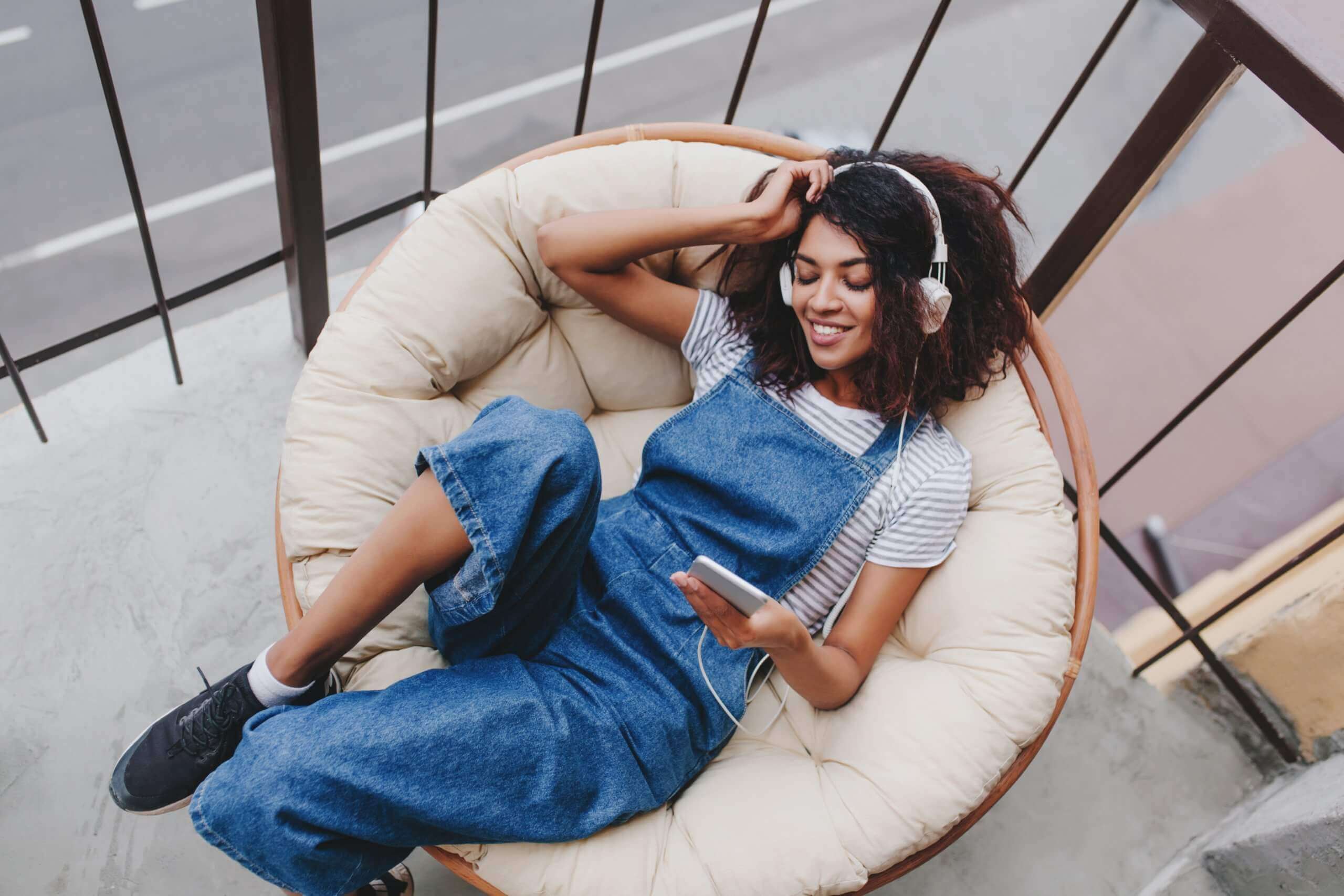 pleased_black_girl_wearing_trendy_sport_shoes_chilling_chair_balcony_enjoying_morning_alone_or-scaled